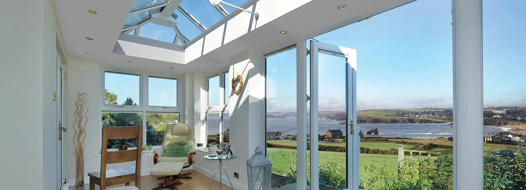 Orangery with a glazed roof lantern and white French doors opening to a coastal view